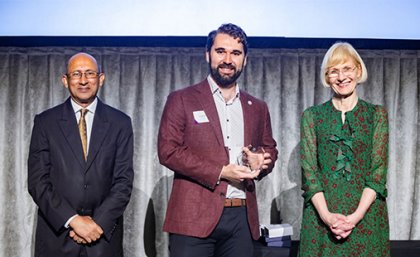 2024 UQ Indigenous Educator Award for Teaching Excellence winner Dr Jared Miles (centre) with Chancellor Peter Varghese AO (left) and Vice Chancellor Deborah Terry AC (right). Three people standing on a stage, one of them holding a trophy